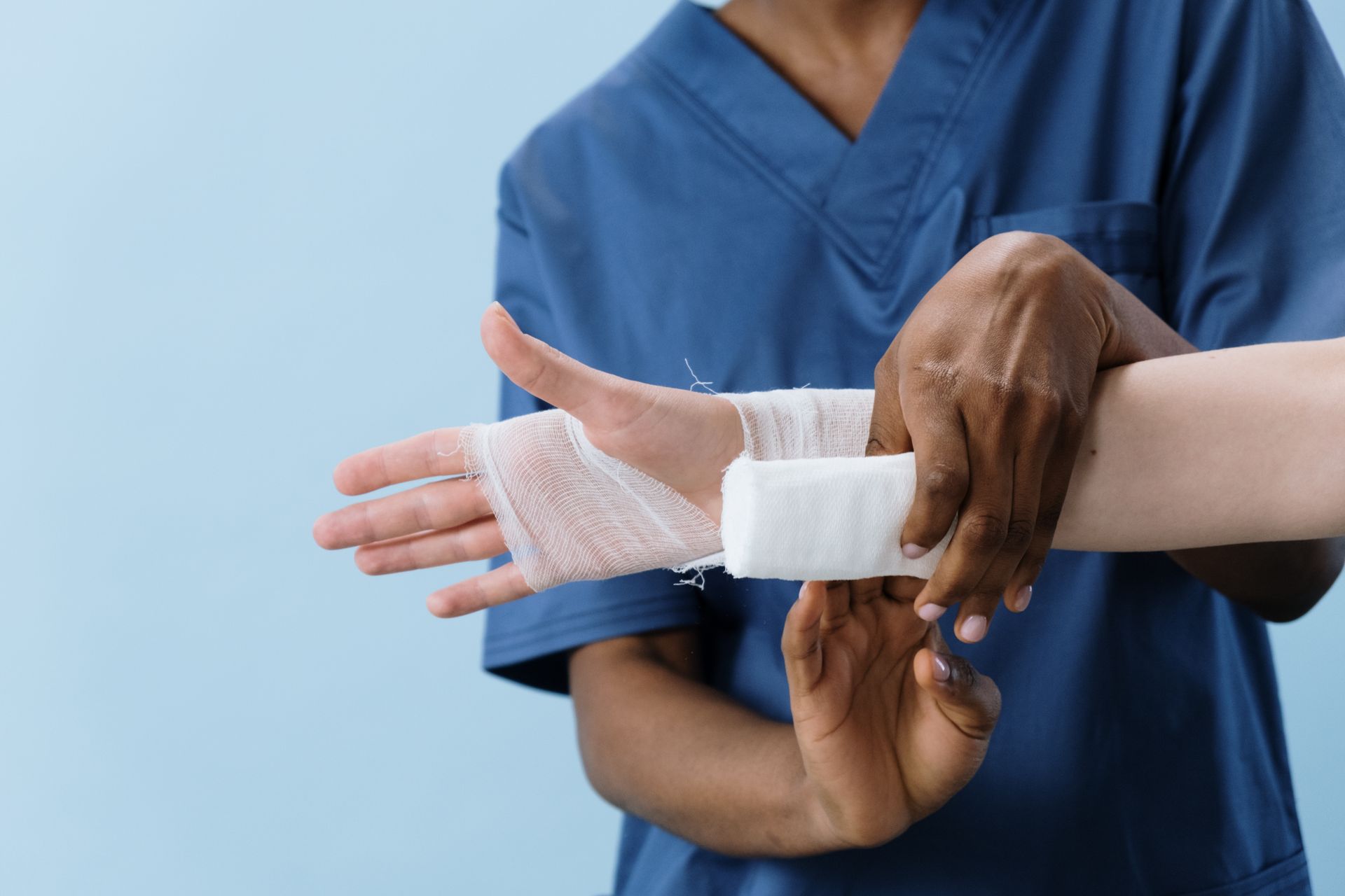 Healthcare worker in scrubs wrapping a patient's injured hand and wrist with gauze